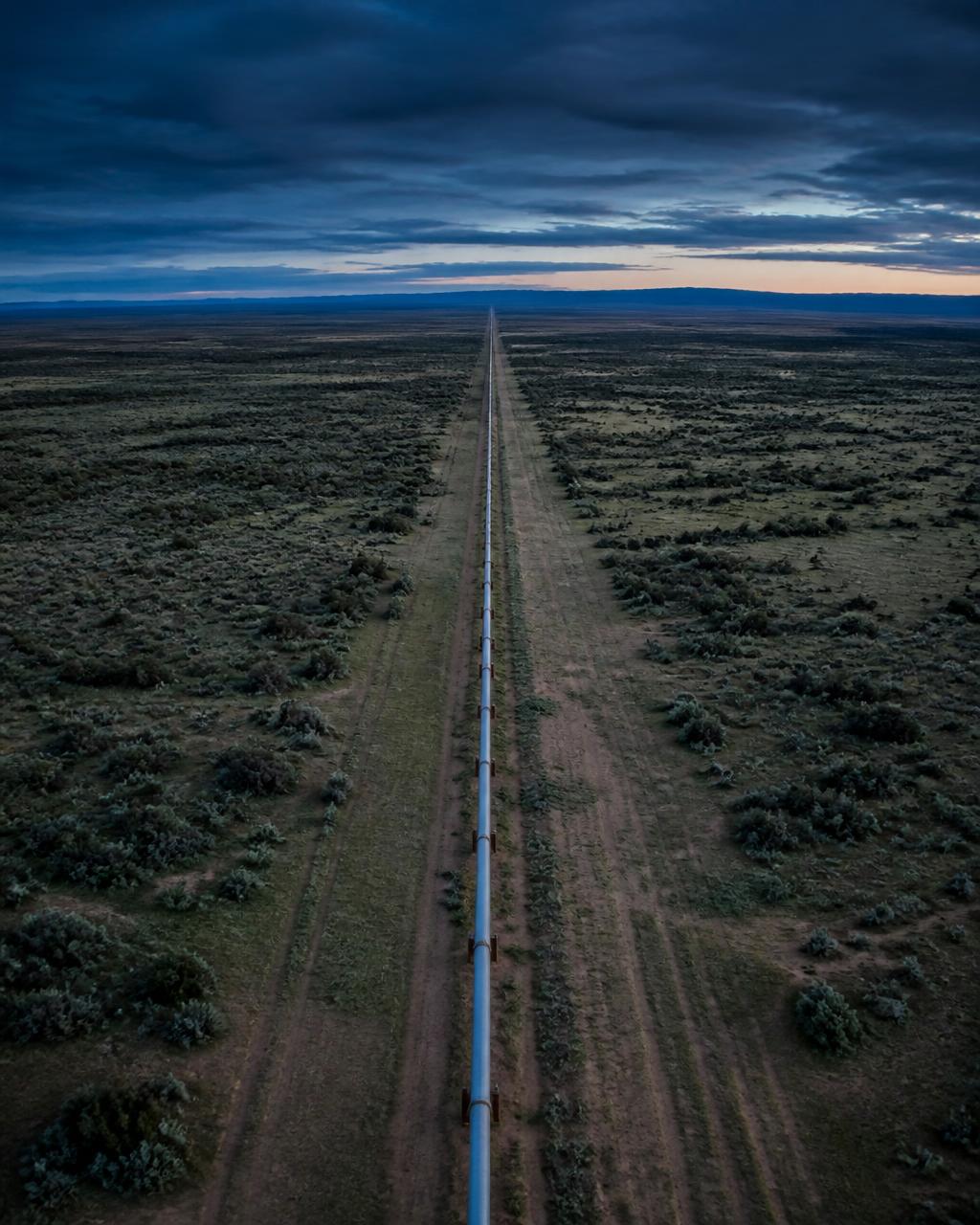 A pipeline corridor running across open terrain at dusk.